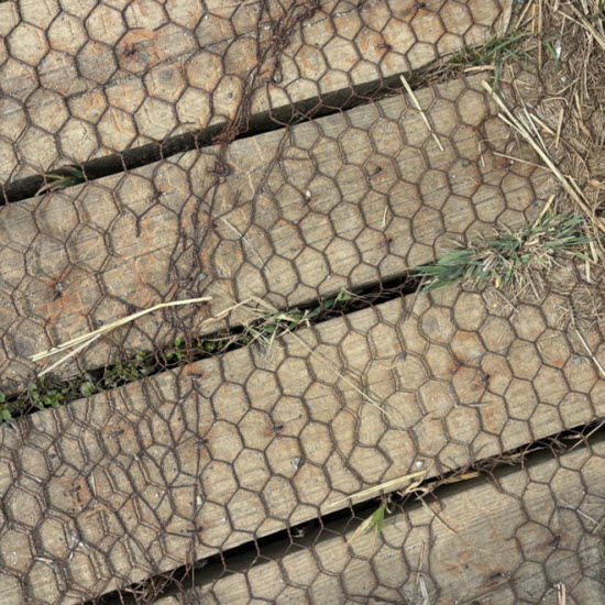 Rusty chicken wire on timber decking, showing distorted mesh and uneven joins